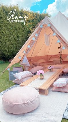 a teepee tent with pink cushions and pillows on the ground in front of it