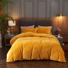 a bed with yellow comforter and pillows in a room next to a plant on the floor