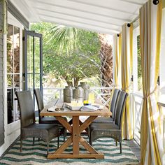 a table and chairs on a porch with yellow curtains