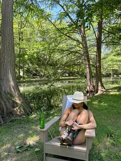 a woman in a hat sitting on a chair next to a tree with a bottle