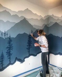 a woman is painting a mountain mural on the wall