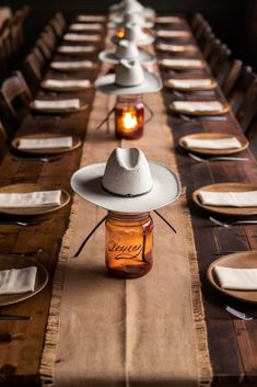 a long table is set with mason jars and cowboy hats on it, along with place settings