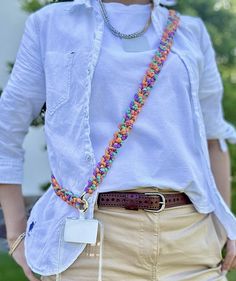 a woman in white shirt and tan skirt holding a cell phone with colorful beads on it