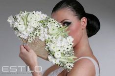 a woman holding a bouquet of flowers and a fan over her face while posing for the camera