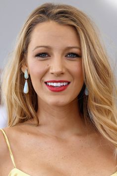 a woman with long blonde hair and blue eyes smiles at the camera while wearing earrings