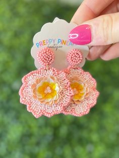 a pair of pink and yellow earrings with flowers on them are being held up by a woman's hand