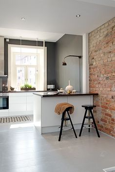 two stools sit in front of the kitchen counter and sink, with an open brick wall behind it