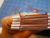 a person holding up several small books with wires attached to them, in front of a cutting board