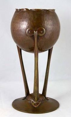 a metal vase with two legs and a face on it's side, sitting on a white surface