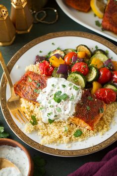 a white plate topped with salmon and vegetables next to a bowl of ranch dressing on top of couscous