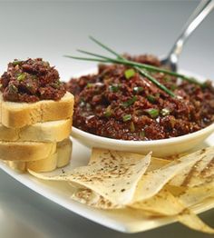 a white plate topped with toasted bread covered in chili and chips next to a bowl of salsa