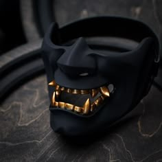 a black mask with gold teeth and fangs on it's face is sitting on a table