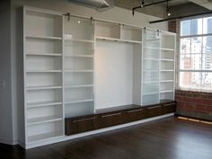 an empty room with white bookcases and wooden floors in front of a brick wall