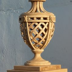 a large wooden vase sitting on top of a stone pillar in front of a white wall