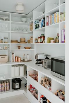 a kitchen with white shelving and lots of food on the counter top in front of a microwave