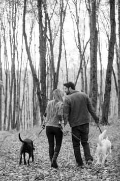 a man and woman walking their dogs through the woods in black and white with leaves on the ground