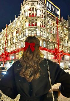 a woman standing in front of a large building with a red bow on her head