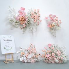 flowers are arranged on the wall next to a sign and easel with a drawing board