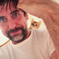 a man with a cat on his shoulder is looking at the camera while he holds his head