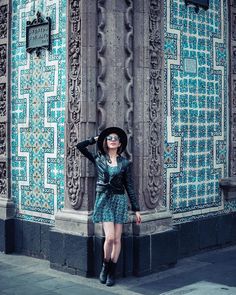 a woman standing in front of a building wearing a black hat and sunglasses with her arms behind her head