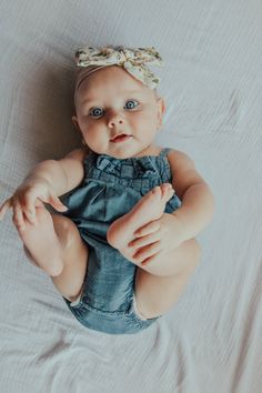 a baby sitting on top of a bed wearing a blue romper and a headband