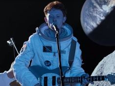 a man in an astronaut's suit singing into a microphone while holding a guitar