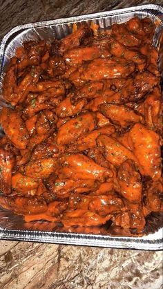 chicken wings covered in gravy sitting on top of a metal pan next to a marble counter