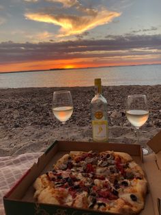 two glasses of wine and a pizza on the beach at sunset with water in the background