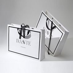 two white shopping bags with black bows on the front and one has a logo on the back