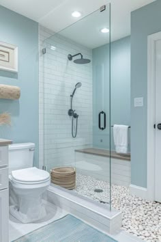 a white toilet sitting next to a walk in shower under a bathroom mirror and light blue walls