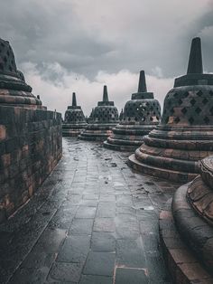 the walkway is lined with stone sculptures on it's sides and there are dark clouds in the sky above