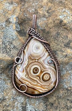 a wire wrapped pendant is sitting on a rock