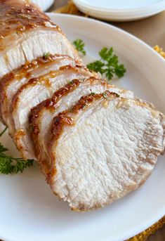 sliced pork sitting on top of a white plate next to sauce and parsley sprigs