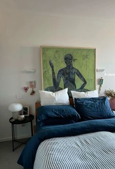 a bedroom with a painting on the wall above the bed and blue linens in front of it