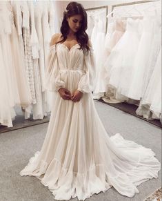 a woman standing in front of a rack of wedding dresses