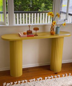 a yellow table with two vases and flowers on it in front of a window