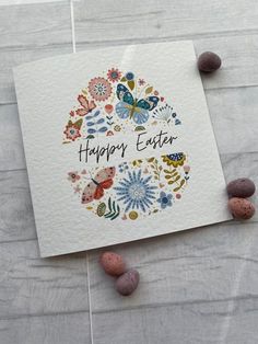 a happy easter card with flowers and butterflies on it next to some rocks in the background