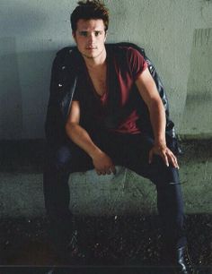 a man sitting on top of a chair wearing black pants and a red t - shirt