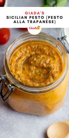 a jar filled with yellow sauce next to a spoon and some tomatoes on the side