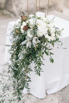 white flowers and greenery are arranged on the back of an outdoor ceremony chair at a wedding