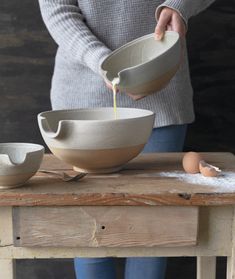 a person pouring something into a bowl on top of a wooden table next to bowls