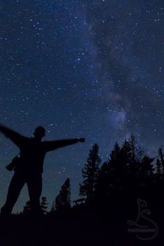 a man standing on top of a hill with his arms outstretched in front of the night sky