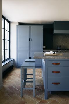 a kitchen with blue cabinets and stools next to a counter top on tile flooring