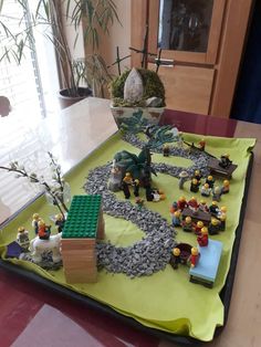 a table topped with legos on top of a green tray covered in rocks and plants