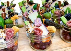 several small glass jars filled with different types of appetizers and fruit on skewers