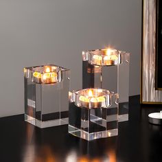 three clear candles sitting on top of a black table next to a candle holder and mirror