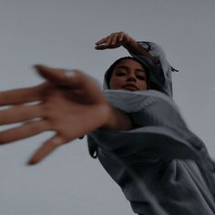 a woman with her hands extended up in the air while wearing a gray hoodie