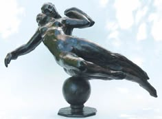 a bronze statue of a man leaning on a ball with his back to the camera