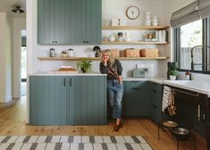 a woman standing in a kitchen next to an oven and counter top with lots of cupboards