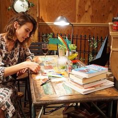 a woman sitting at a table with lots of books on top of it in front of a lamp